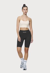 Top corto beige claro con tirantes finos y logo; pantalones cortos de ciclismo negros de cintura alta; calcetines blancos con logo; zapatillas grises con estampado.