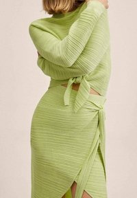 Limonkowy, żebrowany dwuczęściowy zestaw składający się z swetra związanego w talii i spódnicy o kroju wrap z bocznym rozcięciem, wykonany z miękkiego, teksturowanego materiału.