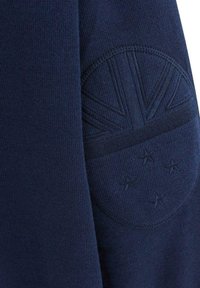 Un sweat-shirt bleu marine avec un patch texturé orné d'une étoile et d'un motif rayé, fabriqué en matériau doux et extensible.