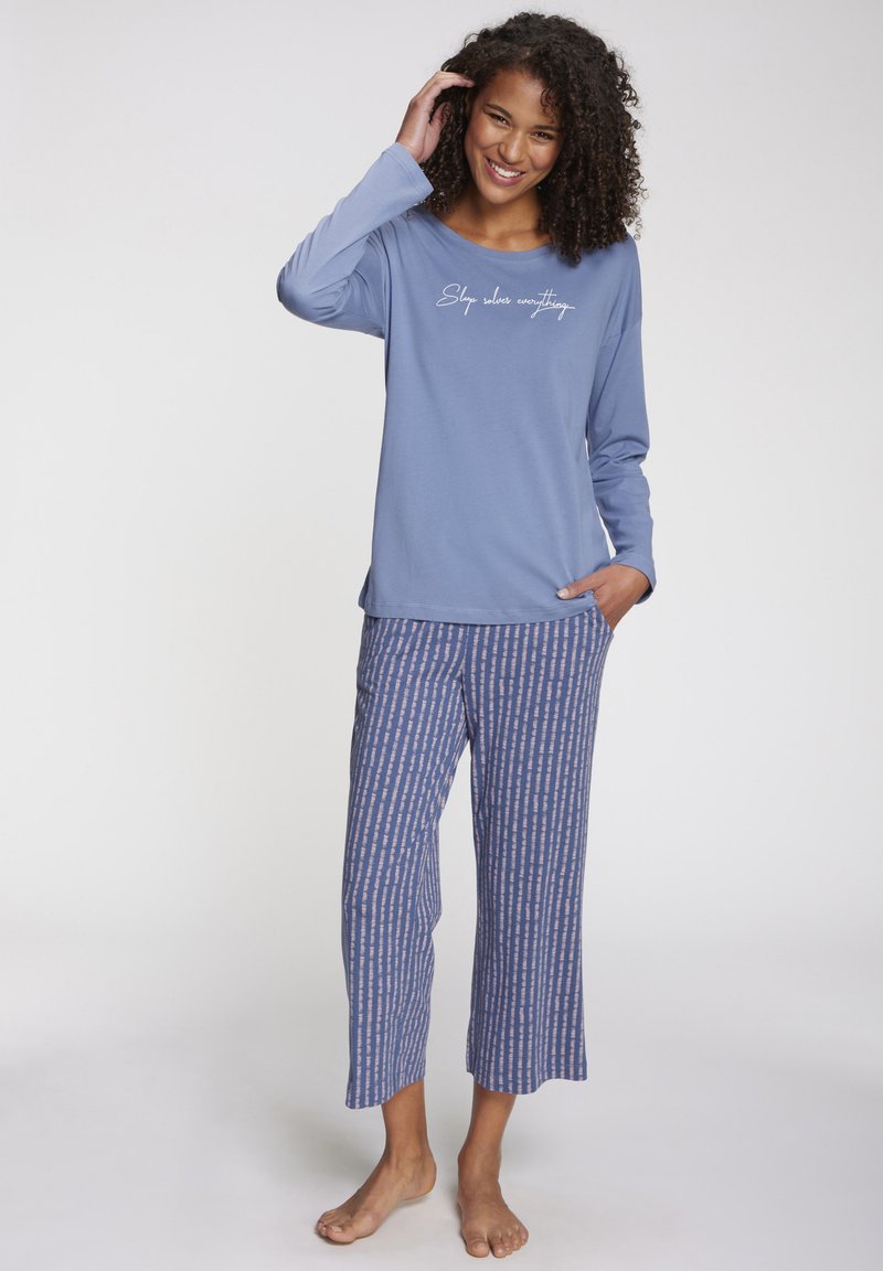 Blue long-sleeve top with white text "Sleep solves everything," paired with patterned blue and pink cropped pants, soft fabric, relaxed fit.