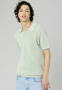 Polo shirt tricoté vert clair avec un col, des manches courtes et un motif texturé, associé à un short en denim bleu clair.