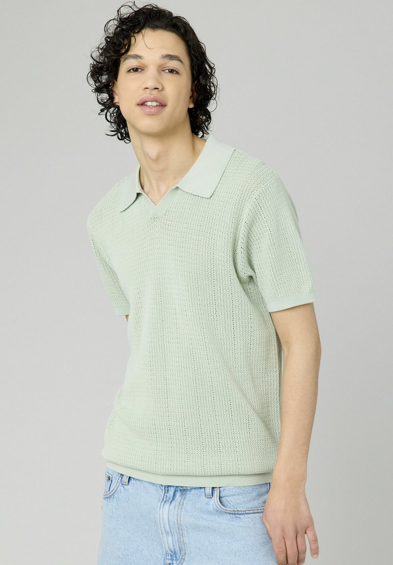 Polo shirt tricoté vert clair avec un col, des manches courtes et un motif texturé, associé à un short en denim bleu clair.