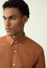 Põlenud oranž nööpidega särk terava kraega, valgete nuppudega ja väikese brodeeritud logoga vasakul rinnal. Sile, kerge kangas.