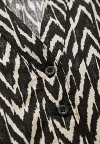 Hemdbluse mit schwarzem und weißem Zickzackmuster, aus strukturiertem Stoff und einem schwarzen Knopf, der mit "Street One" beschriftet ist.