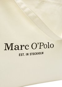 Sac en tissu couleur crème avec une bandoulière cousue et le texte noir "Marc O’Polo EST. À STOCKHOLM" à l'avant.