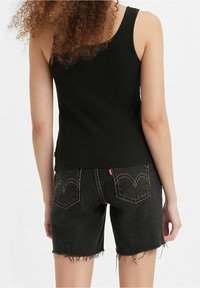 Débardeur noir côtelé associé à un short en denim foncé, avec des ourlets effilochés et des coutures contrastantes sur les poches arrière.