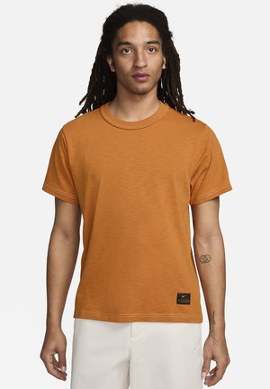 Orange bomulds t-shirt med korte ærmer og rund hals. Har en syet søm og et lille sort Nike-logo patch nederst til venstre.