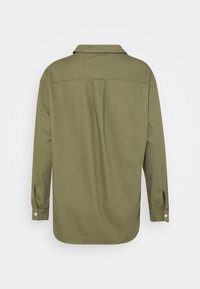 Oliwkowa koszula z długim rękawem, z kołnierzykiem, mankietami na guziki i luźnym krojem. Posiada centralny plis na plecach, co zwiększa swobodę ruchów.