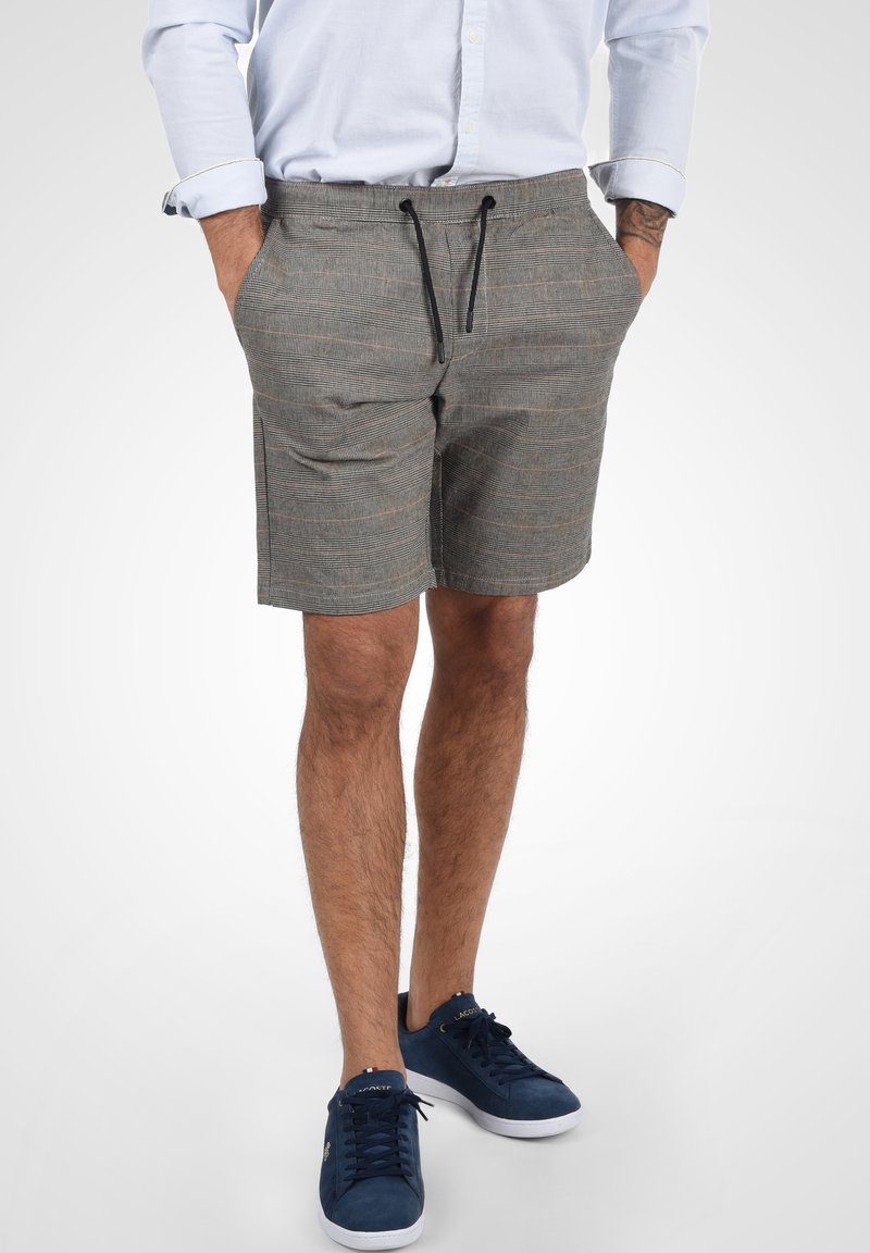 Grå shorts med ett subtilt rutmönster, med dragsko i midjan, sidofickor och en avspänd passform. Bärs med blå sneakers.