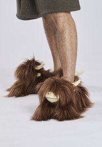 Braune, flauschige Hausschuhe, die einem cartoonhaften Tier ähneln, mit weichen Hörnern und einem runden Gesicht. Sie bestehen aus einem strukturierten Stoff mit langen, haarähnlichen Strähnen.