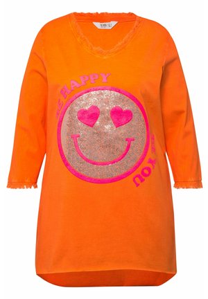 Oranje oversized tuniek met een v-hals, franjes en een centrale graphic van een glimlachend gezicht met hartjes en de tekst "Wees Gelukkig Wees Jijzelf."