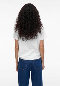 Witte t-shirt met korte mouwen gezien vanaf de achterkant, gecombineerd met hoge blauwe spijkerbroeken met achterzakken en een klassieke snit.