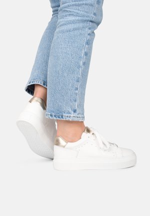 Witte sneakers met een gestructureerde stof, metalen gouden accenten op de hiel en platte rubberen zolen, gecombineerd met lichtblauwe opgerolde jeans.
