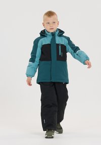 Zweifarbige Kinderjacke in Türkis und Schwarz, aus strapazierfähigem Material, mit Kapuze, Reißverschlusstasche und elastischen Bündchen. Trägt man mit schwarzen Hosen.