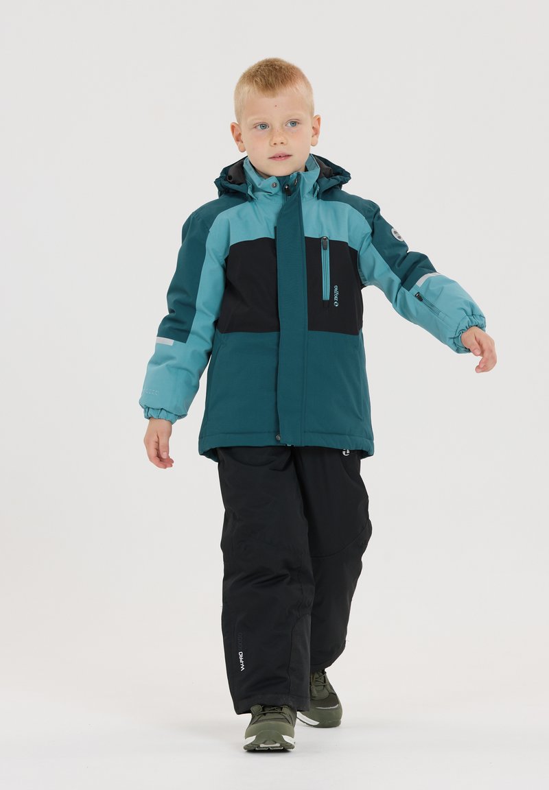 Zweifarbige Kinderjacke in Türkis und Schwarz, aus strapazierfähigem Material, mit Kapuze, Reißverschlusstasche und elastischen Bündchen. Trägt man mit schwarzen Hosen.