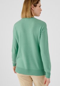 Suéter verde de punto con cuello redondo, puños y dobladillo acanalados, que presenta un corte relajado y una textura suave. Diseño liso sin patrones.