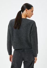 Maglione grigio a maglia, design corto, texture a coste, maniche larghe. Abbinato a pantaloni grigi scuri con tasche posteriori. Semplice e moderno.