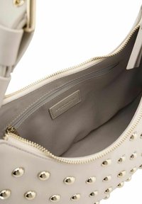 Sac à main beige avec des accents à clous dorés, fermeture éclair et texture lisse. L'intérieur est doublé d'un tissu clair avec une poche zippée.