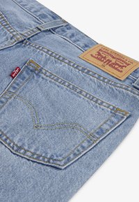 Lyseblå denim jeans med et brunt lædermærke, kontrasterende gule syninger og et rødt logo-tag på baglommen.