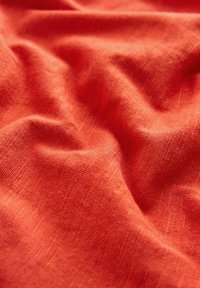 Tekstureret orange stof med et blødt, vævet udseende. Overfladen viser subtile variationer og folder, hvilket indikerer et let materiale.