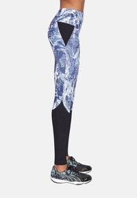 Legginsy z wysokim stanem w niebiesko-biały kwiatowy wzór z czarnym teksturowanym panelem na udzie, zestawione z czarnymi butami sportowymi.