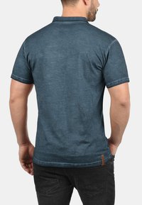 Kortærmet polo shirt i en falmet blå farve, lavet af blødt stof med en struktureret overflade, der har krave og syede detaljer.