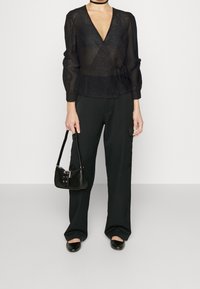 Top a maniche lunghe nera con texture e scollo a V profondo, abbinato a pantaloni neri a gamba larga e una piccola borsa nera. Design morbido e minimalista.