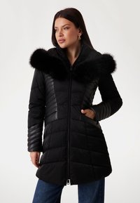 Black puffer coat featuring a zip closure, vertical and horizontal quilted patterns, and a faux fur collar. Design includes side pockets.