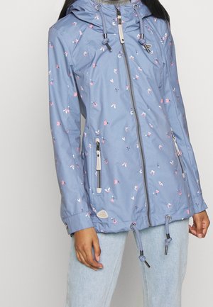 Femme portant une veste à capuche bleu clair avec un petit imprimé floral rose et blanc, fermeture éclair à l'avant, cordons au bas et à la capuche.