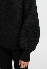 Zwart gebreid sweater met een gestructureerd patroon en volumineuze mouwen, voorzien van geribbelde boorden en een losse pasvorm. Het materiaal lijkt dik en warm te zijn.