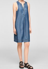 Džínové šaty bez rukávů ve středně modré barvě, s véčkovým výstřihem na knoflíky a volným střihem, s jemnými švy podél lemu.