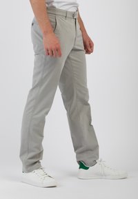 Chinos in cotone grigio chiaro con vestibilità dritta, passanti per cintura e tasche laterali, abbinati a sneakers bianche con dettagli verdi.