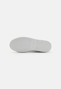 Vit gummisula med ett texturerat mönster, med "Calvin Klein"-logotypen i mitten. Slät yta med rundade kanter.
