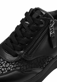 Basket noire avec un mélange de cuir et de tissu texturé. Les caractéristiques incluent des lacets noirs plats, une fermeture éclair sur le côté, et des accents à imprimé léopard.