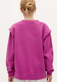 Lyserød sweatshirt med en afslappet pasform, som har teksturerede ærmer og diskret blomsterbroderi på venstre manschet.