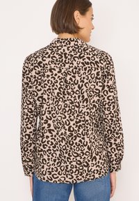 Košile s leopardím potiskem v béžové barvě s černými skvrnami, dlouhé rukávy, manžety na knoflíky, zadní yoke detail a volný střih, spárovaná s modrými džíny.