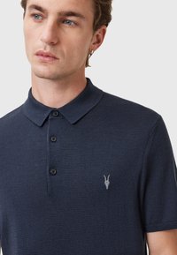 Marine poloshirt gemaakt van textuurstof, met een klassieke kraag, een knoopsluiting met drie knopen en een klein geborduurd ontwerp op de borst.