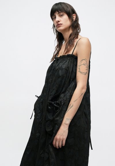 Μαύρο αμάνικο φόρεμα με υφή υφάσματος, σιγμενόμενη μέση και πλαϊνές τσέπες. Διαθέτει κορδόνι στο ντεκολτέ και στο τελείωμα.