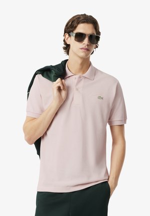 Camisa polo de suave tela rosa, con cuello clásico, mangas cortas y un logo verde bordado. Texturizada con patrones sutiles.