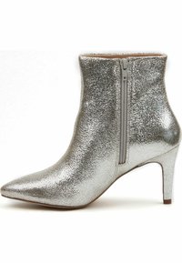 Bottine métallique argentée avec une finition texturée, bout pointu et fermeture éclair à l'arrière. Présente un talon mince pour l'élévation.