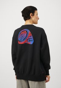 Fekete pulcsi, amelyen egy színes rózsa látható kör alakú mintával a hátoldalán. Rózsás mandzsetták és alsó szegély. Nike logó elöl.