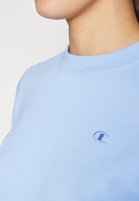 Sudadera de color azul claro hecha de tejido suave, con un escote redondo y un pequeño logotipo bordado en el pecho.