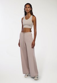 Jasno beżowy krótki top i luźne, jasnoróżowe spodnie dresowe z elastycznym pasem i sznurkiem, w zestawieniu z wzorzystymi sneakerami.