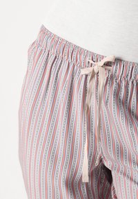 Gestreepte pyjamabroek in tinten roze, blauw en wit met een elastische tailleband en een strikdetail aan de voorkant. Zachte stoftextuur.