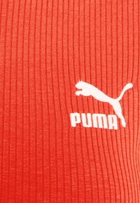 Il tessuto a coste rosso presenta un logo PUMA bianco con il nome del marchio sottostante. La texture è liscia con una leggera lucentezza.
