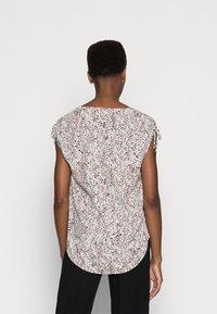 Haut ample à manches courtes en tissu blanc texturé avec un motif abstrait coloré. Comprend des liens sur les côtés des manches et un ourlet arrondi.