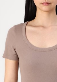 Ribadee, lühikeste varrukatega tipp helepruunis, ümmarguse dekolteega ja sileda tekstuuriga. Minimalistlik disain ilma nähtavate kaunistusteta.
