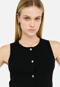 Black ribbed knit tank top with a round neckline, featuring five gold-tone skull buttons down the front. Smooth texture, fitted shape.