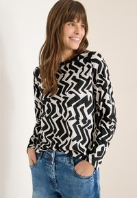 Sort og hvid langærmet top med abstrakt mønster, rund halsudskæring, blødt stof og afslappet pasform. Båret med lyseblå jeans.