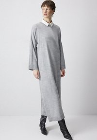 Rochie gri cu mânecă lungă și guler ascuțit, realizată dintr-un material texturat. Asortată cu cizme scurte negre, cu vârful ascuțit. Design simplu, minimalist.